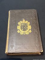 Front cover of antique book showing embossed brown leather cover with gold crest, some spine damage.