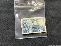 Front view of vintage 1952 American Automobile Association 50th Anniversary 3 cent blue postage stamp in clear protective plastic pouch on black fabric.