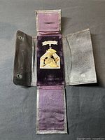 Full view of medal housed in opened black leather foldable case with purple velvet lining, showing the medal centered inside.