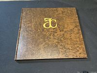 Front cover of the leather-bound art book with gold embossed AC monogram on brown textured leather.