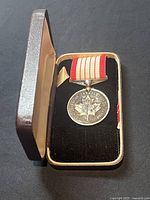 Photo of the open presentation case showing the silver medal with red and white striped ribbon inside.