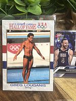 Close-up of Greg Louganis Olympic diving card showing image of him diving at the Olympics with Hall of Fame branding.