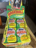 Four sealed packs of 1987 Topps Baseball cards arranged inside the original box, showing front and top flaps with visible branding and color.