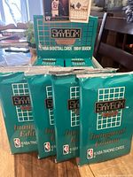 Four sealed 1990-91 SkyBox NBA Basketball Cards Inaugural Edition packs displayed outside the box on a table.