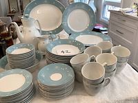 Photo showing full set arranged including plates, cups, saucers, creamer, and teapot with blue rim and floral pattern.