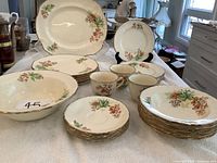 Wide view showing entire Alfred Meakin set including plates, bowls, cups, and large platter arranged on a white towel, clear floral orange berry pattern detail with gold trim visible