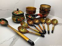 Full set of 14 hand painted wooden pieces arranged in a single photo, showing bowls, spoons, and lidded container with Chohloma styling and color palette