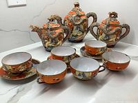Overview showing three lidded teapots, six cups and one cup on a saucer