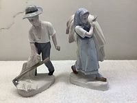 Two Royal Copenhagen porcelain figurines next to each other, boy with hoe and girl carrying sack.