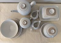 Full view photo showing all 12 pieces laid out on a table including teapot, sugar bowl, creamer, butter dish, bowls, and plates, showcasing set’s design and condition.