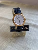 Front view of Lorus vintage wristwatch on original stand with price tag showing $74.95. Gold-tone case and white dial with Roman numerals visible.