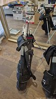 Full view of TaylorMade black golf bag with multiple junior right hand golf clubs inside, standing on floor with reflective mirror behind.