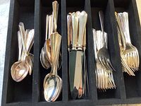 Full shot of assorted silverplated cutlery including spoons, knives, and forks in black velvet-lined wooden storage compartments.
