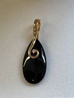 Front view of the polished black onyx teardrop pendant with 14K gold swirl detail and attached gold bail.