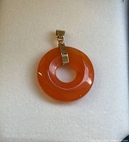 Front view of the vintage 14K gold pendant with smooth polished orange stone in donut shape.