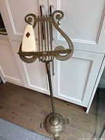 Brass lyre-shaped music stand with metronome placed on sheet holder, front view