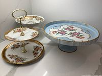 Full view of all three porcelain dessert and cake dishes showing floral designs and gold accents, including three-tier stand and two pedestal plates.