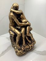 Sculpture viewed from the front showing a nude couple embracing, painted gold with visible paint wear.
