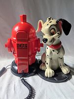 Front view of the red fire hydrant phone base with black text reading '$101 Dalmatians' and the Dalmatian dog figure standing beside it on a black base.