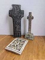 Two Celtic crosses (one large silver-colored metal, one smaller) with rectangular wax relief plaque on the floor in front, showing size and detail of designs.