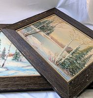 Two framed winter landscape paintings stacked, both signed by Orvokki Jalava. Frames show wear and tear.