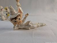Reclining elf or pixie figure lying on side, glossy ceramic with hand-painted face and costume, approx. 2.5 inches tall.