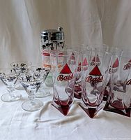 Photo showing the full set of Bass Ale glasses with distinctive red triangle bases paired with cocktail glasses and shaker behind.