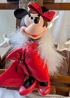 Front view of Minnie Mouse doll in red satin dress with sparkling details and white feather boa, showing figure and outfit clearly.