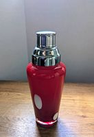 Front view of red glass cocktail shaker with white polkadots and silver metal top, showing overall shape and colors.
