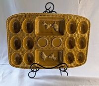 Front view of mustard yellow ceramic devilled egg tray with 12 egg wells and 2 raised rooster figurines in rectangular sections.