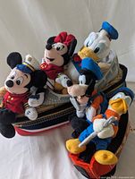 Group of Disney plush characters Mickey, Minnie, Donald, and Goofy sitting in plush cruise ship and train car, showing condition and included characters.
