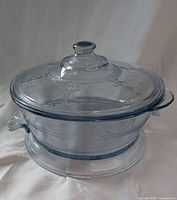 Sapphire blue glass casserole dish with lid and trivet displaying the Philbe pattern from Fire King, photographed on white backdrop