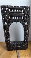 Front view of the dark wood carved frame with cutouts and dragon motifs on the sides