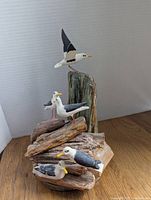 Hand carved and oil painted seagull model depicting several gulls perched and flying over driftwood pieces.