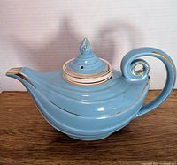 Full side view of aqua blue Hall Aladdin teapot, showing teapot body, spout, lid with finial and handle with gold trim.