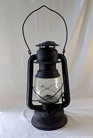 Full view of large black metal lantern lamp with glass globe and carrying handle.