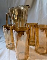 Photo showing marigold-colored glass pitcher with handle and four matching glasses with hexagonal pattern on translucent glass