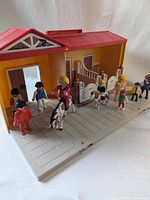 Playmobil stable case open with figures and horses on base showing front and inside of stable.