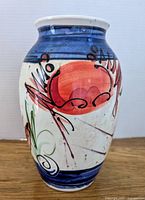 Pottery vase with visible abstract red, black, and green design on cream background with blue bands, showing colorful artwork and condition