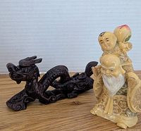 Photo showing resin figurine and wooden dragon side by side on wooden surface against white background.