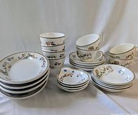 Full view of stack of bowls, cups, saucers, and plates showing the floral and gold trim design on white china.