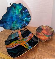 Three vintage art glass dishes displayed on stands and flat, showing shapes, colors, and condition.