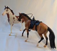 Two Breyerfest 2016 horse models: one matte light bay with black tack, and one white pinto horse.