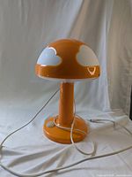 Front view of the orange mushroom-shaped lamp with white clouds and attached cable with missing wall plug.