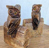Front and side view of the owl bookends showing the yellow glass eyes, carved feathers, and stained alabaster/plaster base shaped like books.