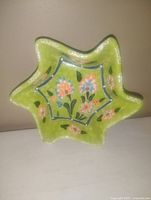 Photo of a green star-shaped ceramic pottery dish with hand-painted pink and blue flowers and green leaves, glossy finish, approximately 5 inches wide.