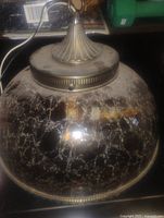 Close-up image showing the amber glass lamp shade with crackled texture and metal hanging fittings.