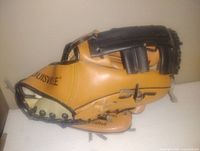 Side view of tan and black leather Louisville baseball glove showing branding and stitching details.