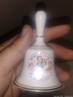 Photo of a white ceramic bell held by hand, showing colorful image of Royal Family and gold trim.
