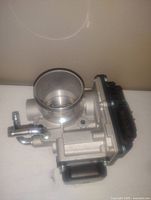 Clear image of the metallic carbonator showing its cylindrical body, pipe connectors, and attached black control assembly.